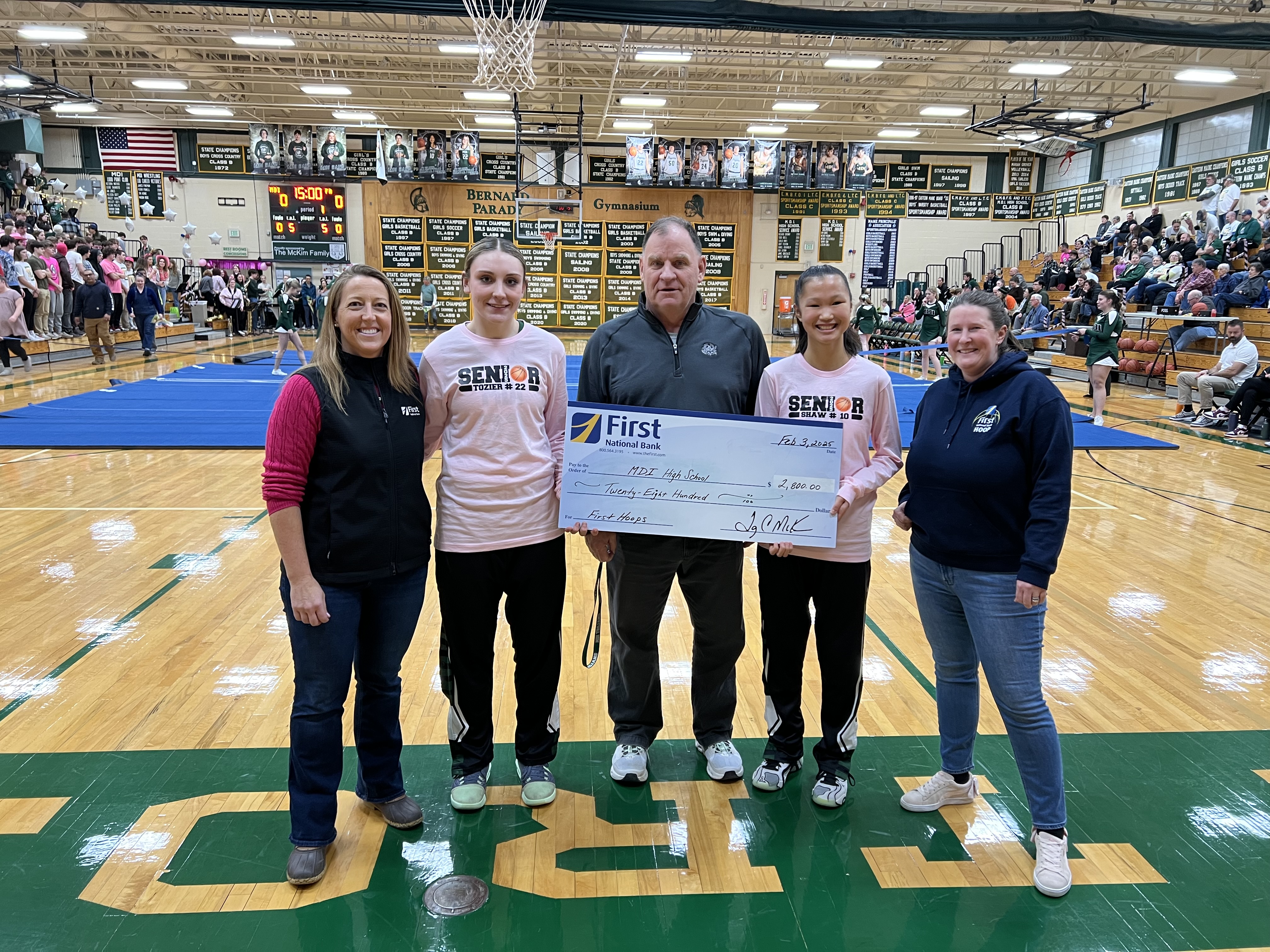 Five people in a school gym holding a a big check