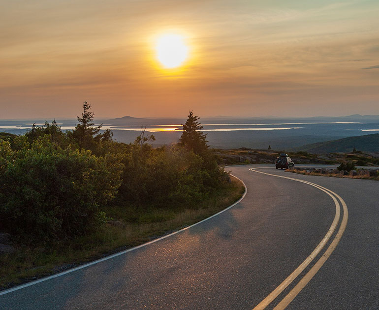 Car driving into sunset on Acadia National Park road
