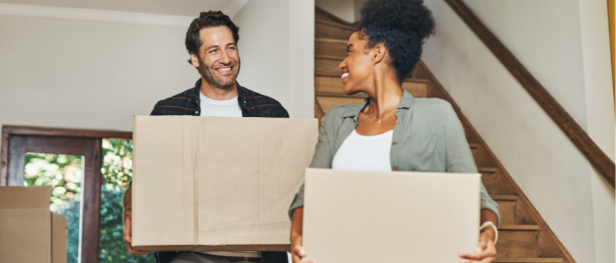 Two people smiling holding moving boxes in new home. 