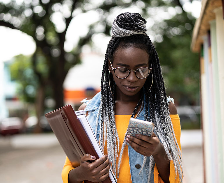 Student looking at phone holding books